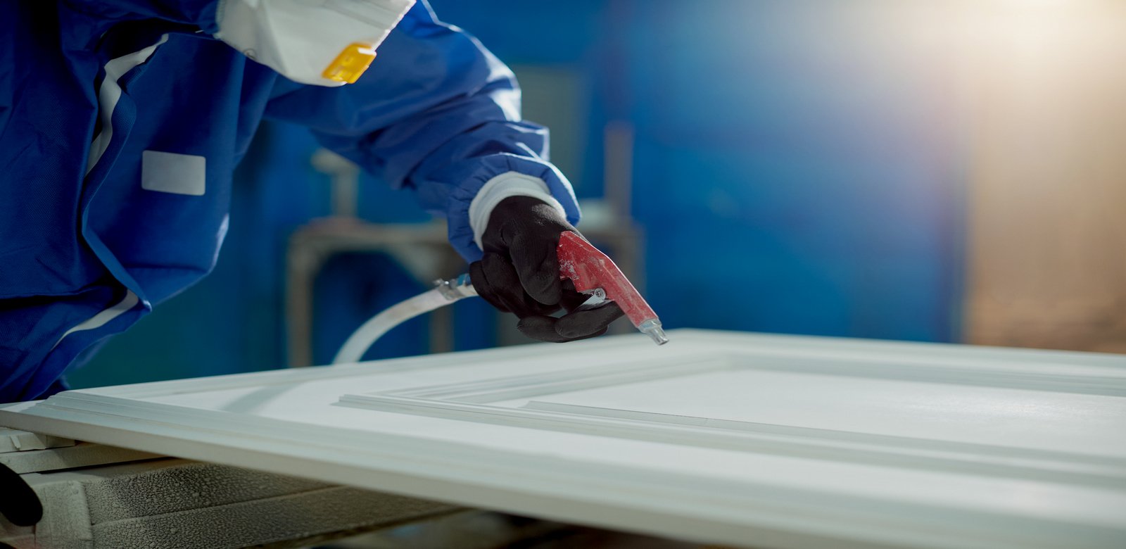 Close-up of worker spraying timber with spray gun and woodworking factory.